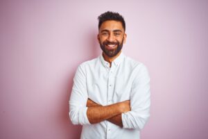 Man in white shirt with arms crossed smiling with pink background